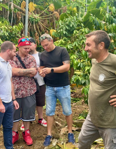 Four people are looking at a flower, under a greenhouse and surrounded by tropical trees.